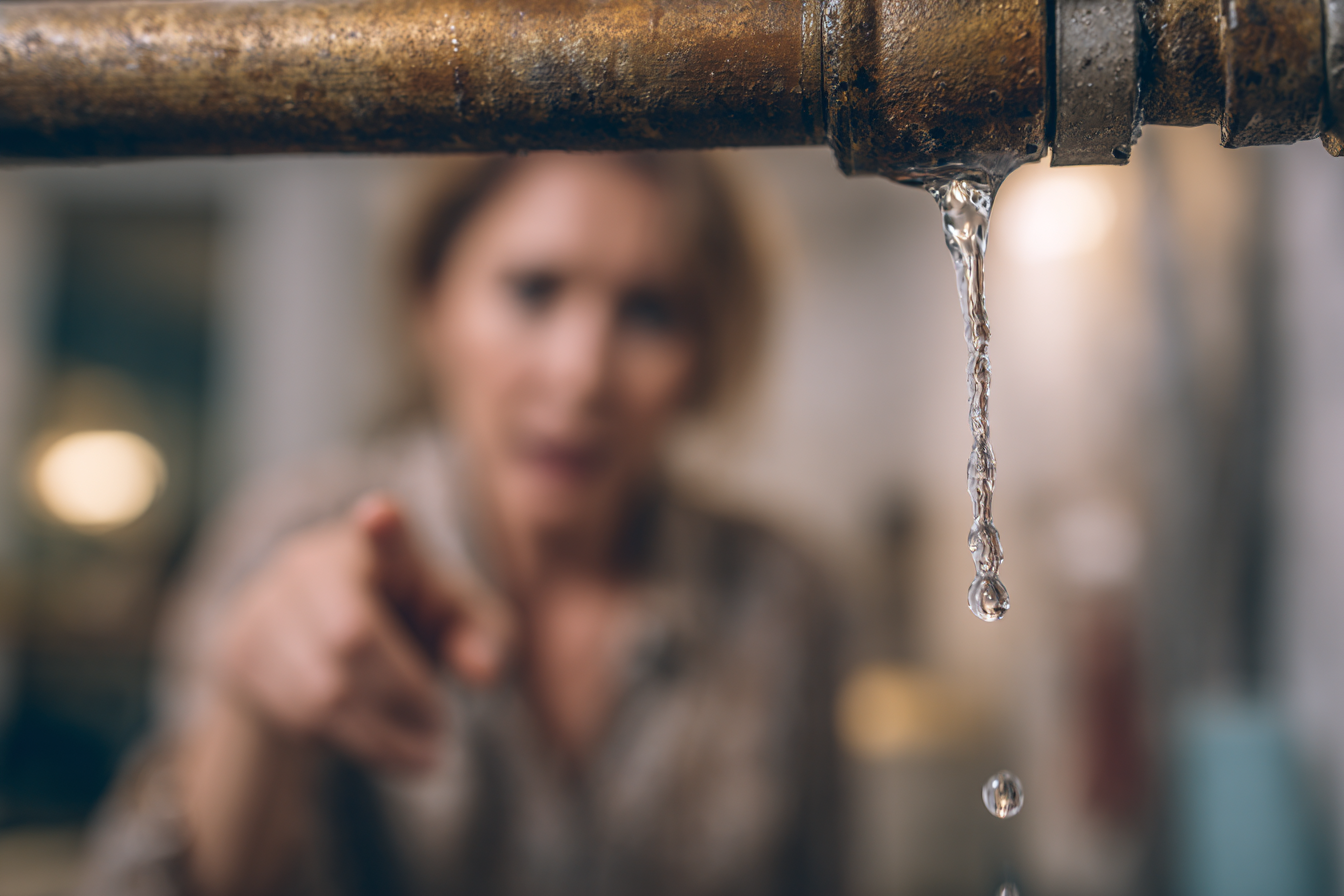 Fuite d’eau visible sur un tuyau domestique, avec une personne montrant la fuite du doigt, image illustrant la nécessité de détecter rapidement les fuites d’eau.